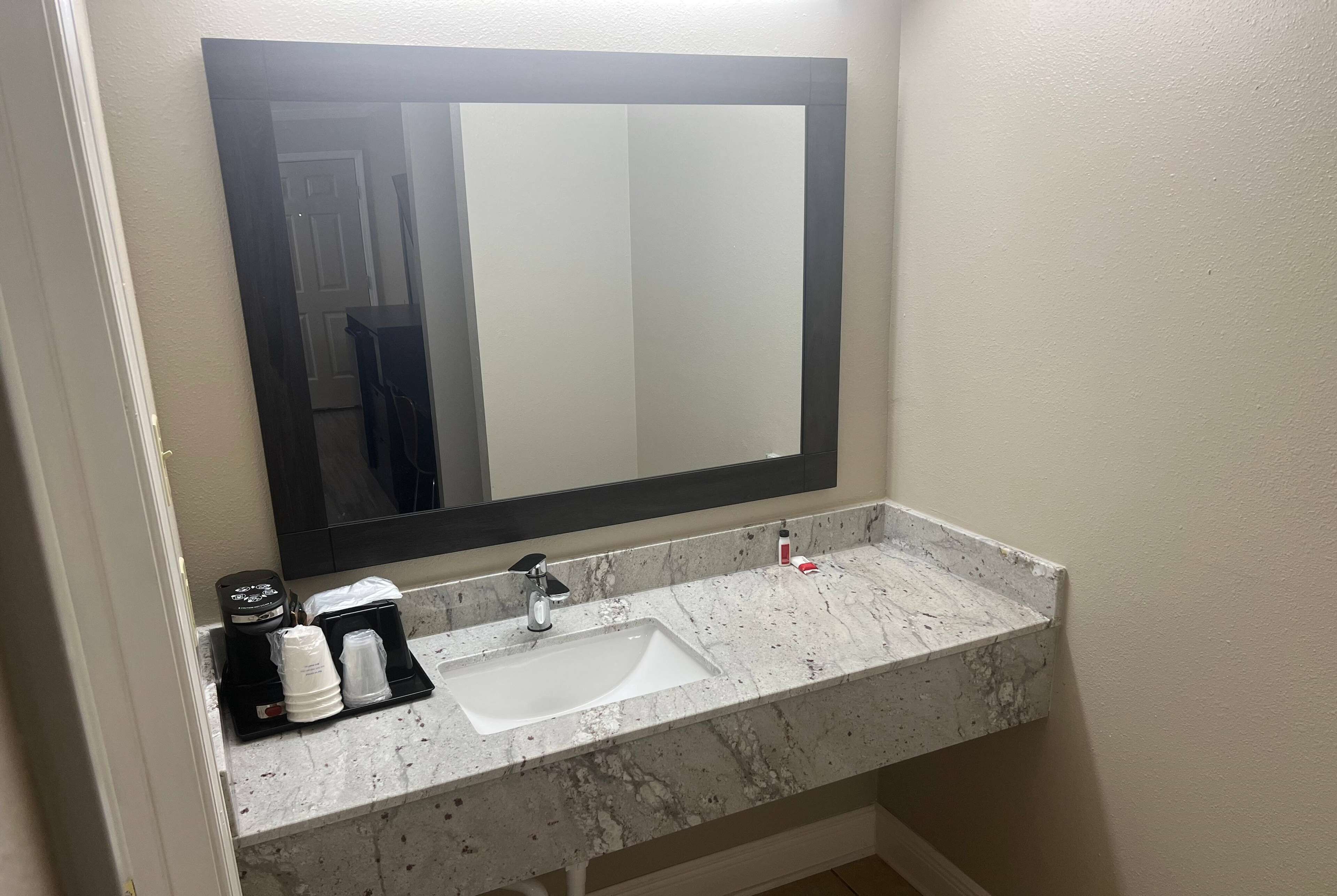 Un baño con un lavabo blanco, un espejo grande y una bandeja negra con artículos de aseo.