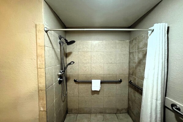 A small, tiled shower stall with a grab bar, a towel rack, and a showerhead.