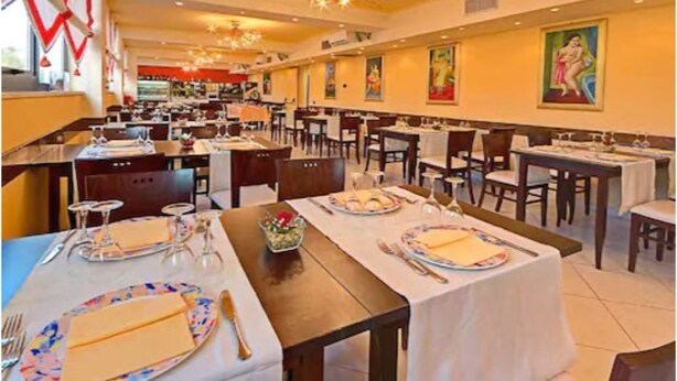 Un restaurante con varias mesas dispuestas, vajilla, sillas y un candelabro.