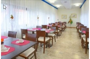 Un salón de conferencias con varias mesas y sillas, cortinas blancas y cuadros en las paredes.