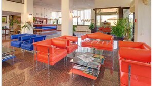 Un vestíbulo con asientos naranja y azul, un mostrador de recepción y una mesa de centro de vidrio con revistas.
