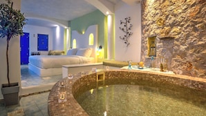 A spa area with a hot tub, a bed, and a stone wall. - Astarte Suites (Santorini)