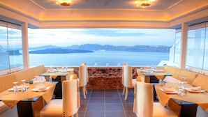 A restaurant with tables set for dining, a stone wall centerpiece, and a view of the sea and mountains. - Astarte Suites (Santorini)