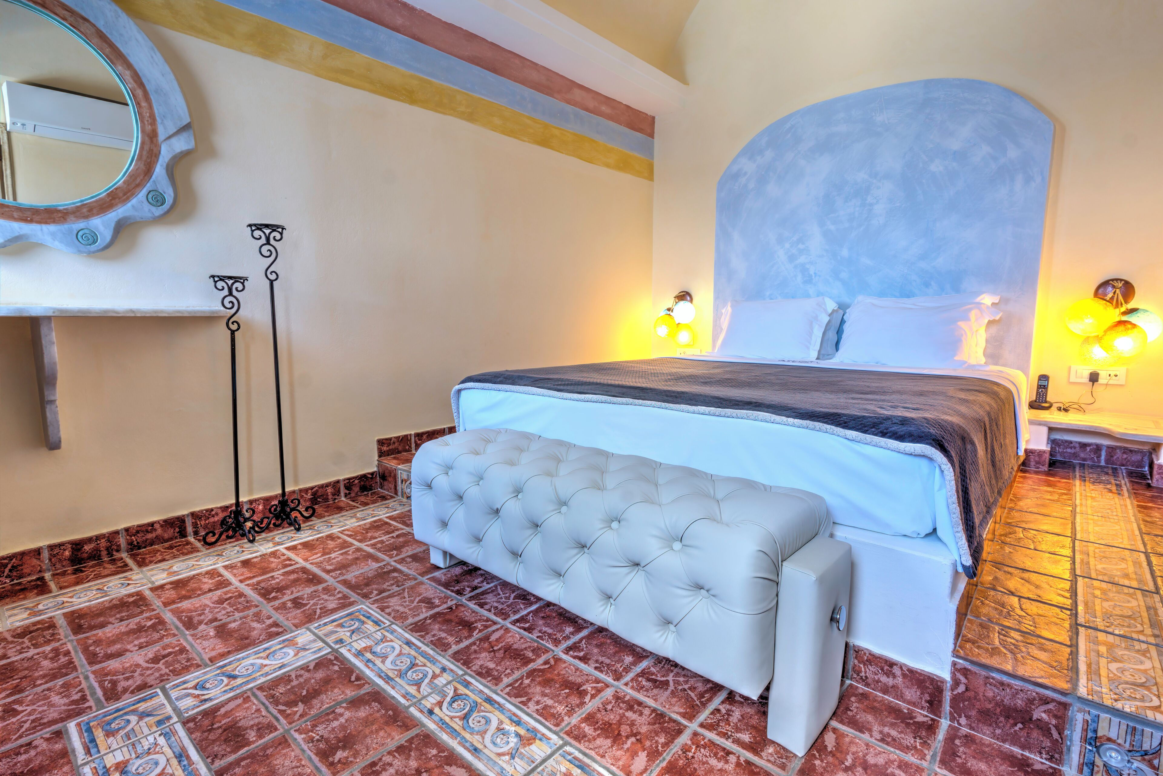 A bedroom with a large bed, a bench, a mirror, and a wall-mounted light fixture.