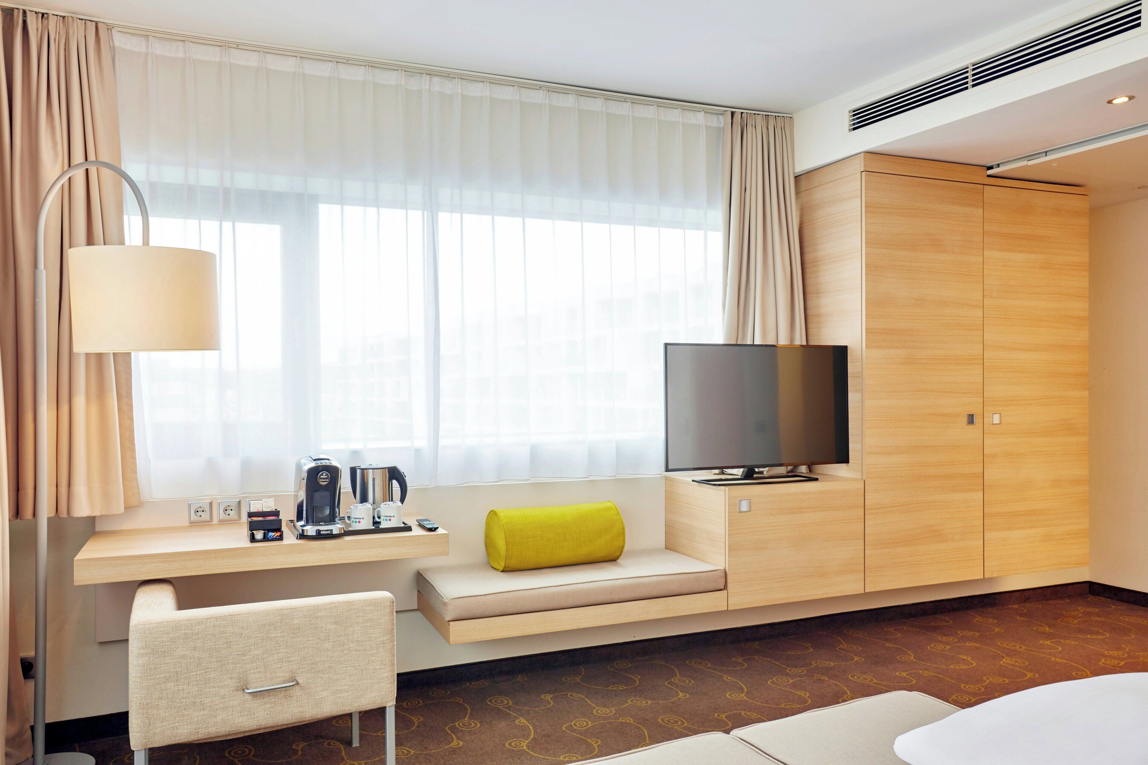 A hotel room with a bed, a TV, a desk with a coffee maker, and a sofa.