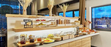 Mostrador de buffet con diversos alimentos y vista a la ciudad a través de la ventana.