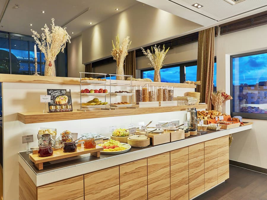 A buffet counter with various food items and a city view through the window.
