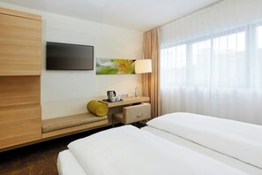 A hotel room with a bed, a desk with a lamp, a television, and a window with curtains. - Hotel Salzburg-Hauptbahnhof (Salzburg)
