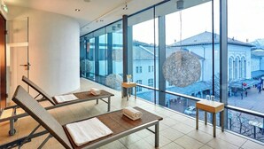 A modern interior with large windows, a seating area with benches, and a view of a historic building outside.