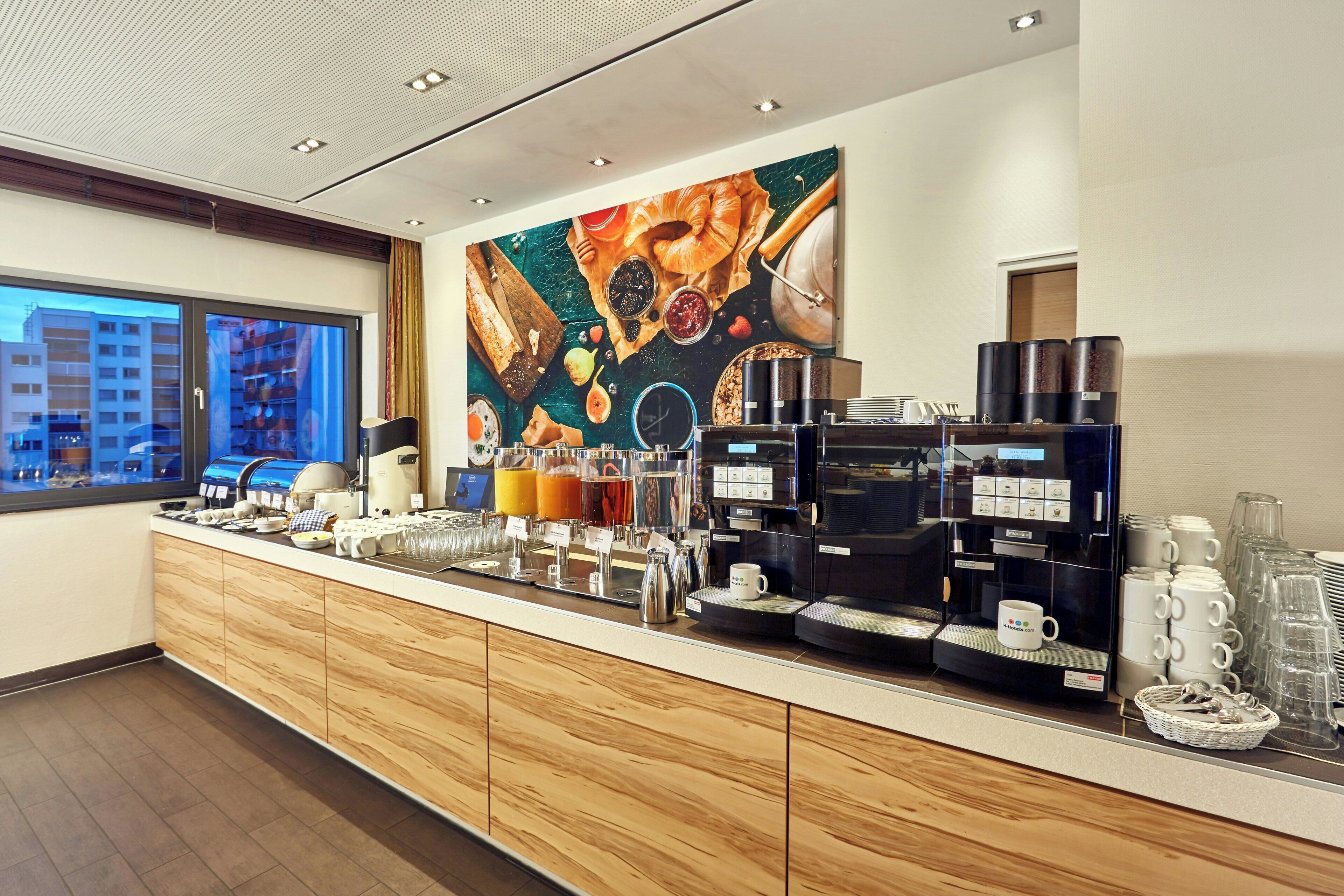 A hotel breakfast area with a large window, a coffee machine, and various breakfast items.