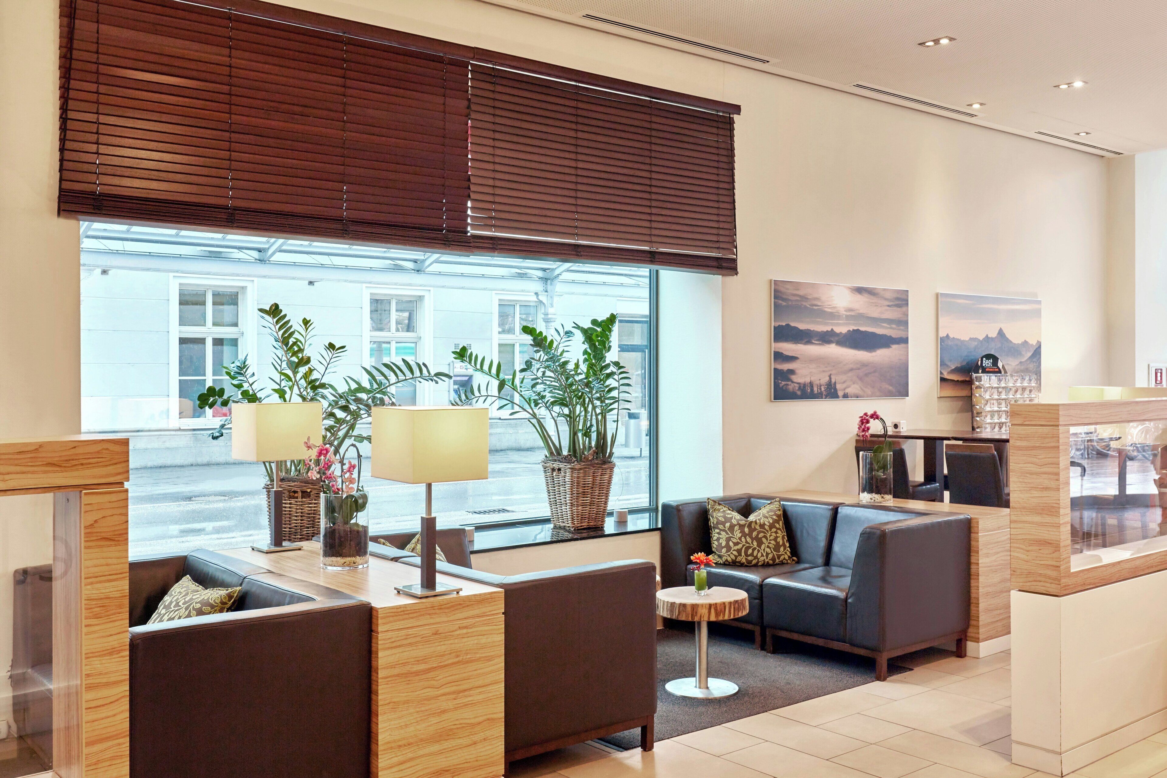 Eine moderne Hotelhalle mit Sitzgelegenheiten, großen Fenstern und dekorativen Pflanzen.