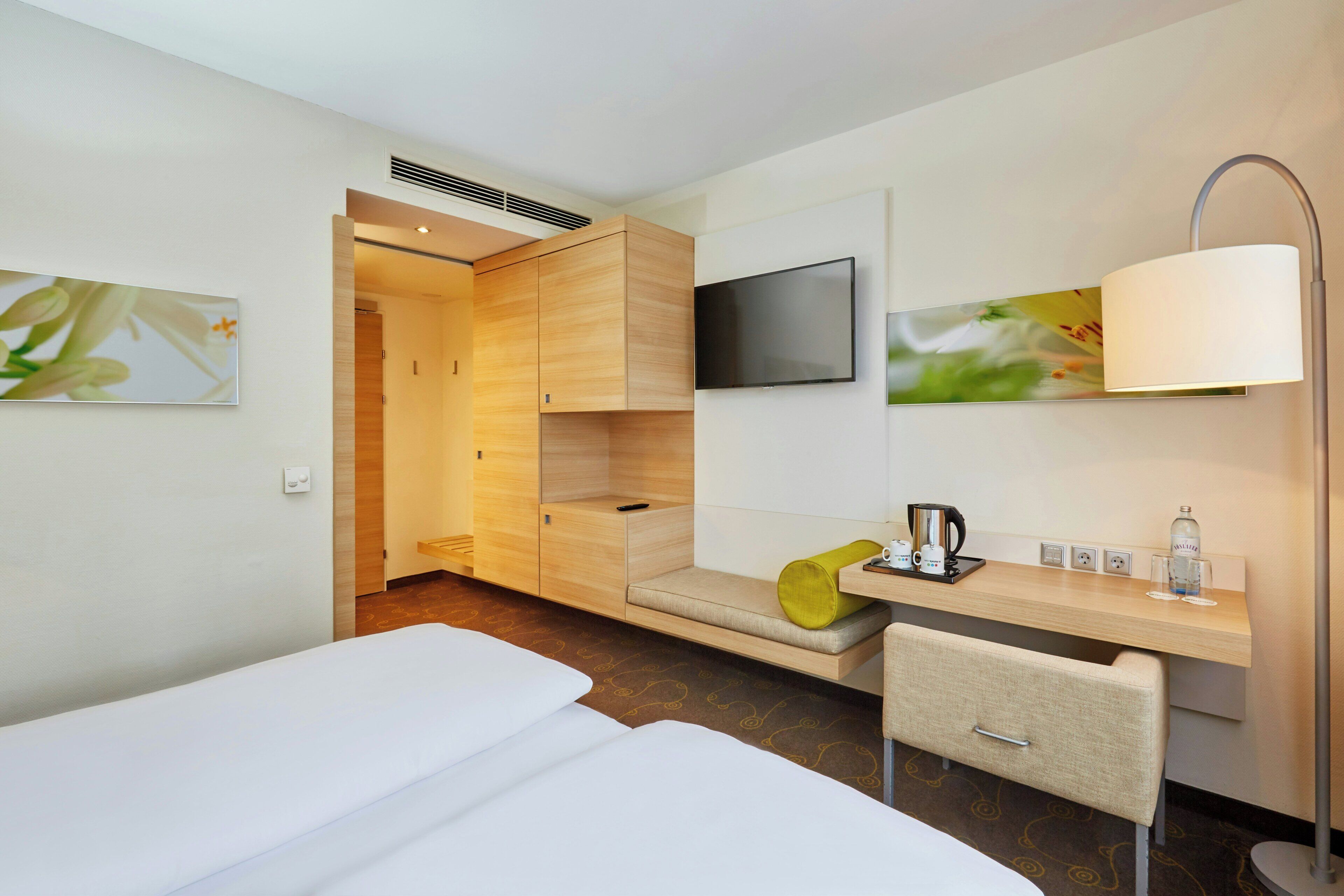 Ein Hotelzimmer mit einem Bett, einem Schreibtisch mit Stuhl, einem Fernseher und einer Lampe.