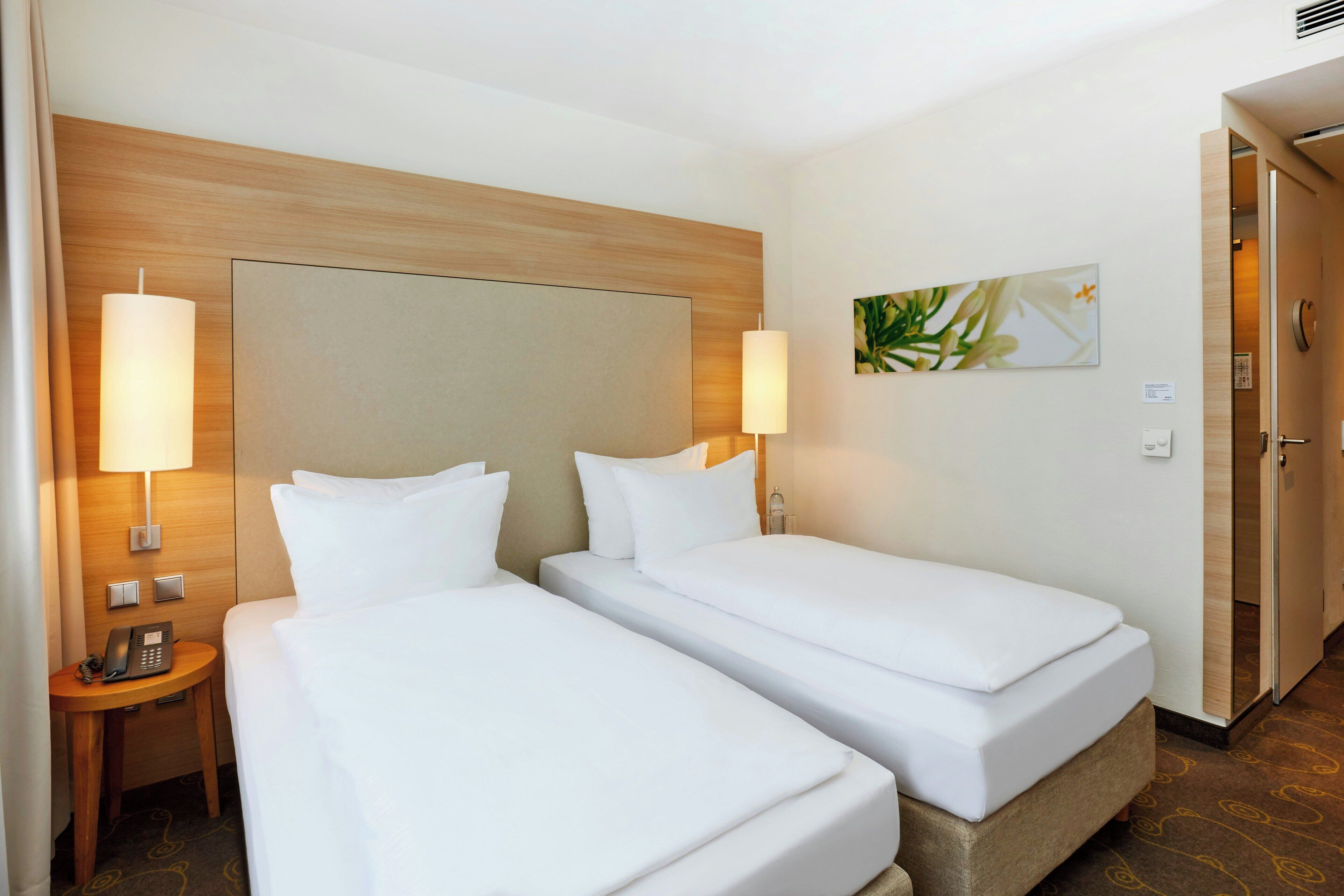 Ein Hotelzimmer mit zwei Einzelbetten, einem Holzkopfstück, Nachttischlampen, einem Telefon und einem Bild an der Wand.