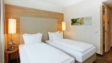 Ein Hotelzimmer mit zwei Einzelbetten, einem Holzkopfstück, Nachttischlampen, einem Telefon und einem Bild an der Wand.