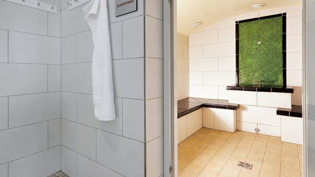 A bathroom with white tiles, a shower with a white towel, a green-tiled window, and a sink with a black countertop.
