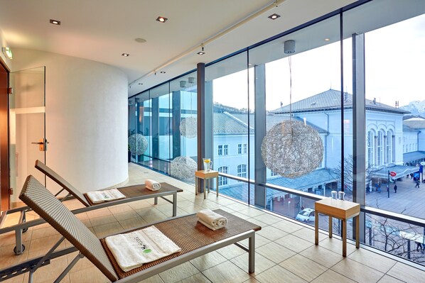 Un moderno espacio de spa con paredes de vidrio, sillones de descanso y vistas a un edificio histórico.