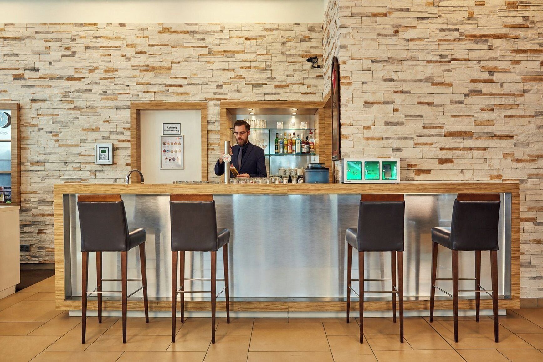 A bar area with a stone wall backdrop, a bar counter, and three bar stools.