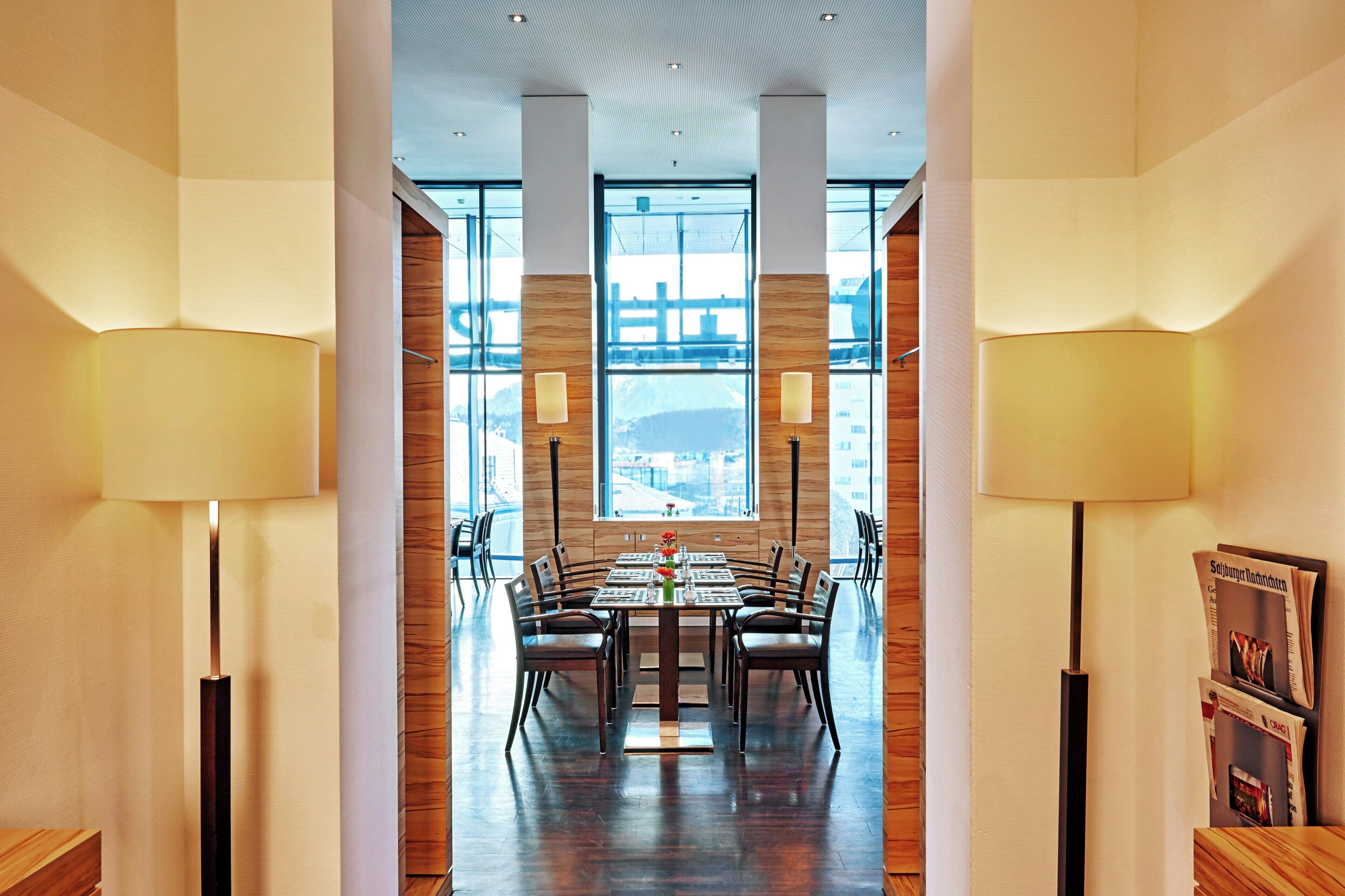 A modern dining area with a long table, chairs, and two floor lamps.