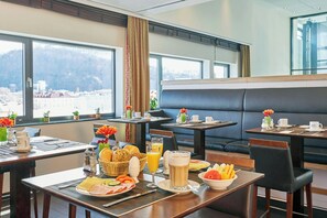 A hotel dining area with tables set for breakfast, including plates of food, drinks, and a view of the mountains through large windows. - Hotel Salzburg-Hauptbahnhof (Salzburg)