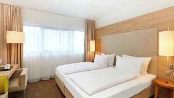 A hotel room with a large bed, two bedside tables, a desk with a chair, and a window with curtains.