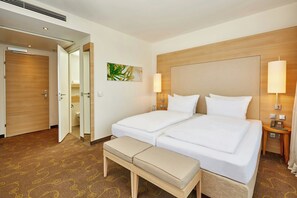 A hotel room with two beds, a bench, a bedside table with a phone, and a wall-mounted lamp. - Hotel Salzburg-Hauptbahnhof (Salzburg)