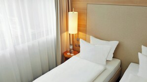 A hotel room with a bed, a nightstand with a lamp, and a window with curtains.