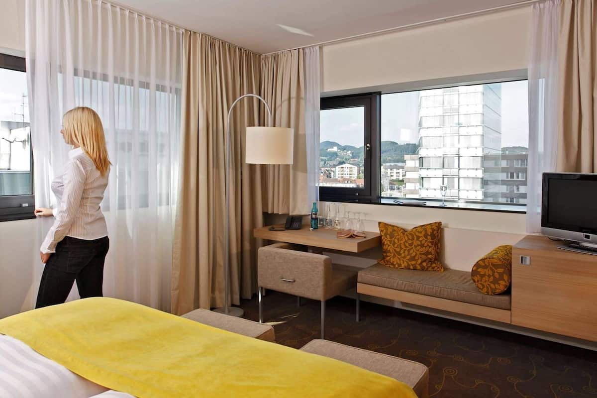 Habitación de hotel con cama, escritorio, televisión y ventana con vista a la ciudad.