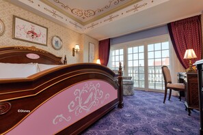 Habitación de hotel con una cama grande, un escritorio con lámpara, una silla y vistas al exterior a través de un ventanal.