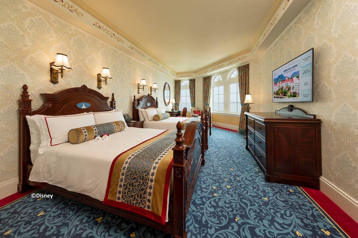 Ein Hotelzimmer mit einem großen Bett, zwei Nachttischen, einem Schminktisch, einem Spiegel und einem an der Wand befestigten Fernseher.