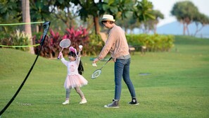 Une personne et un enfant se trouvent sur un terrain herbeux, avec une raquette de badminton et un volant.