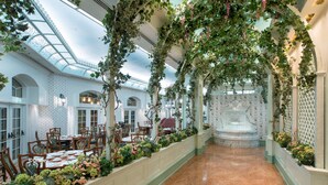 Un espace de restauration intérieur doté d’un plafond en verre, de tables recouvertes de nappes blanches et de chaises.