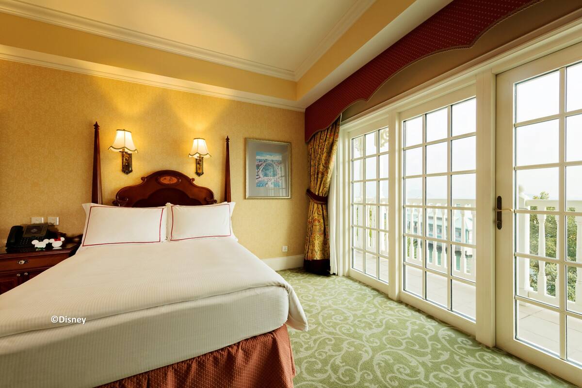 Ein Hotelzimmer mit einem großen Bett, zwei Wandlampen, einem Gemälde und Blick durch ein großes Fenster.