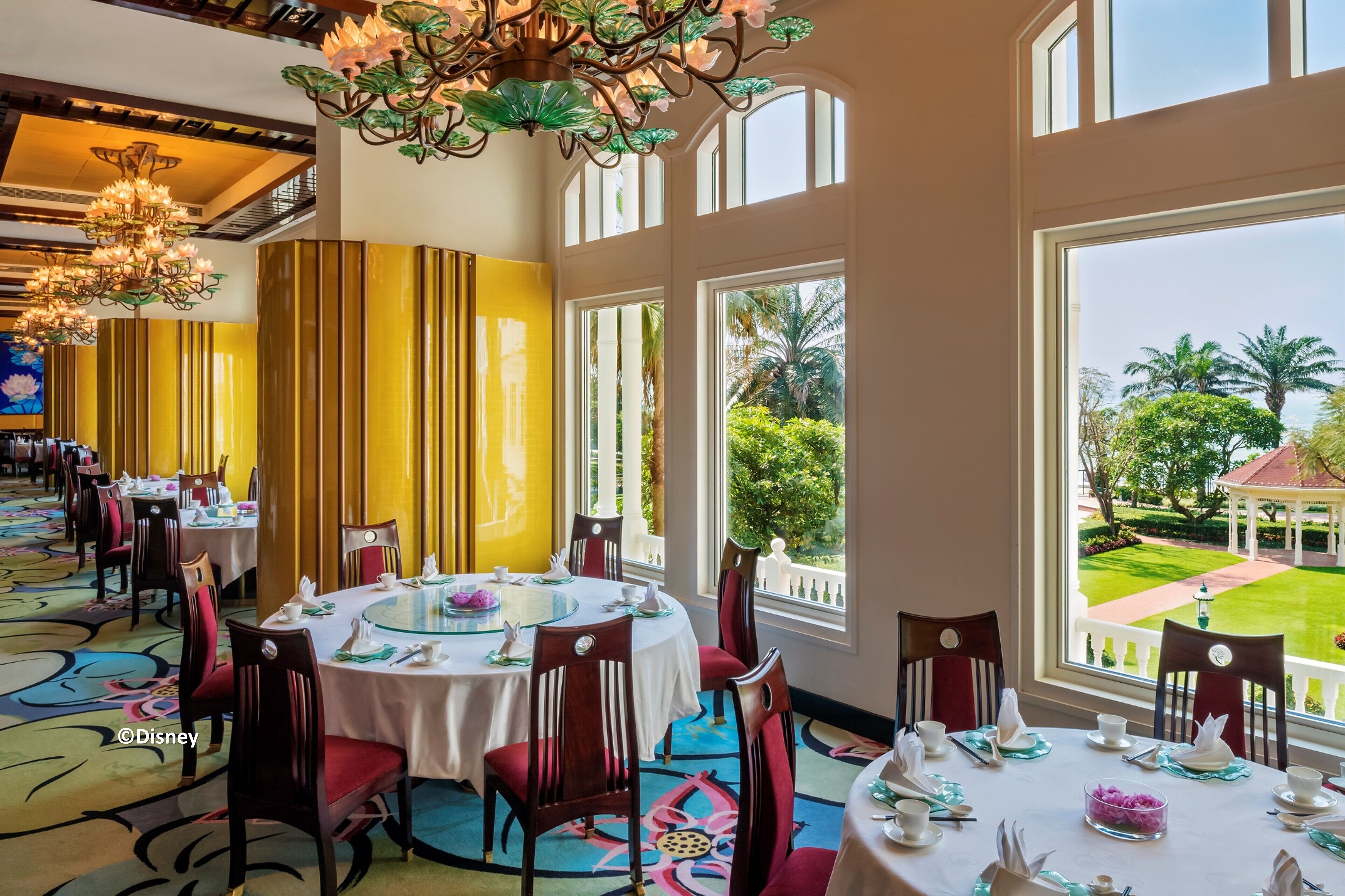 Un restaurant avec des tables rondes, des chaises rouges et une vue sur un jardin.