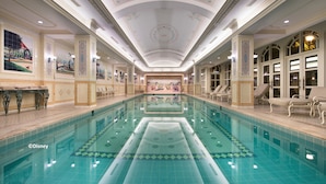 Une grande piscine intérieure dotée d’une fontaine centrale, entourée de chaises longues et agrémentée d’un plafond décoratif.