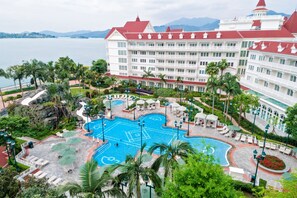 A large hotel with a swimming pool surrounded by palm trees and lounge chairs.