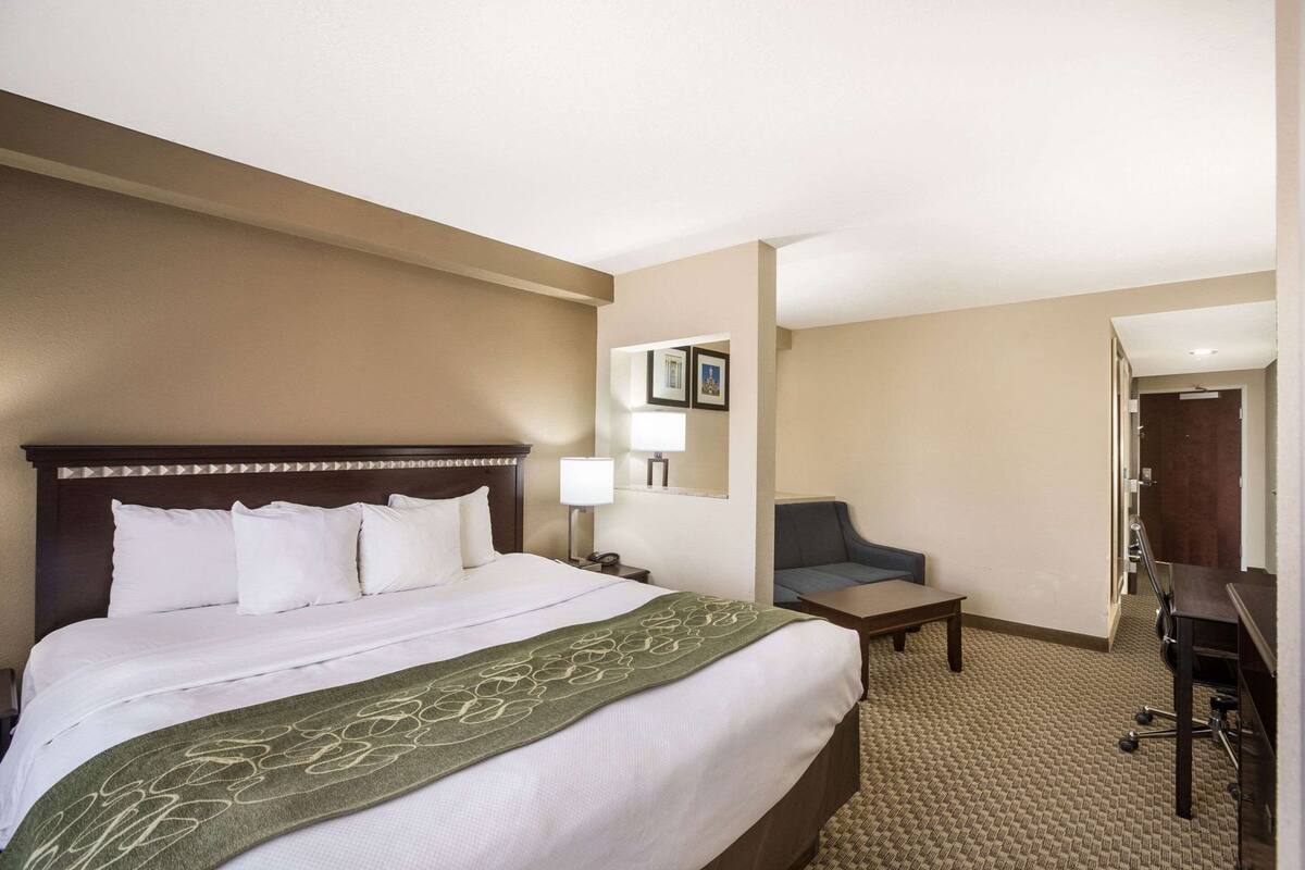 A hotel room with a large bed, a desk, a chair, and a small table.