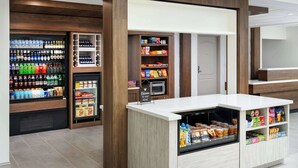 Een zelfbedieningsstation voor eten en drinken met gekoelde opslag en schapruimte, een magnetron en een welkomstbord.