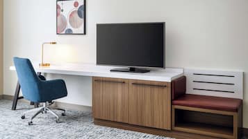 A modern office desk with a flat-screen TV, a blue office chair, and a red cushioned bench.