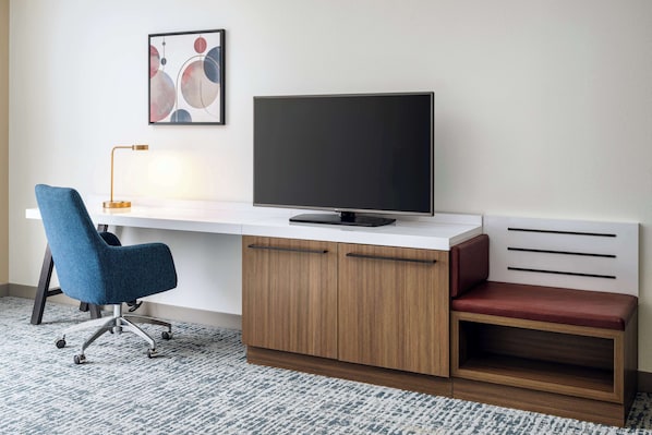 A modern office desk with a flat-screen TV, a blue office chair, and a red cushioned bench. - Hilton Garden Inn Huntsville South/Redstone Arsenal (Huntsville)