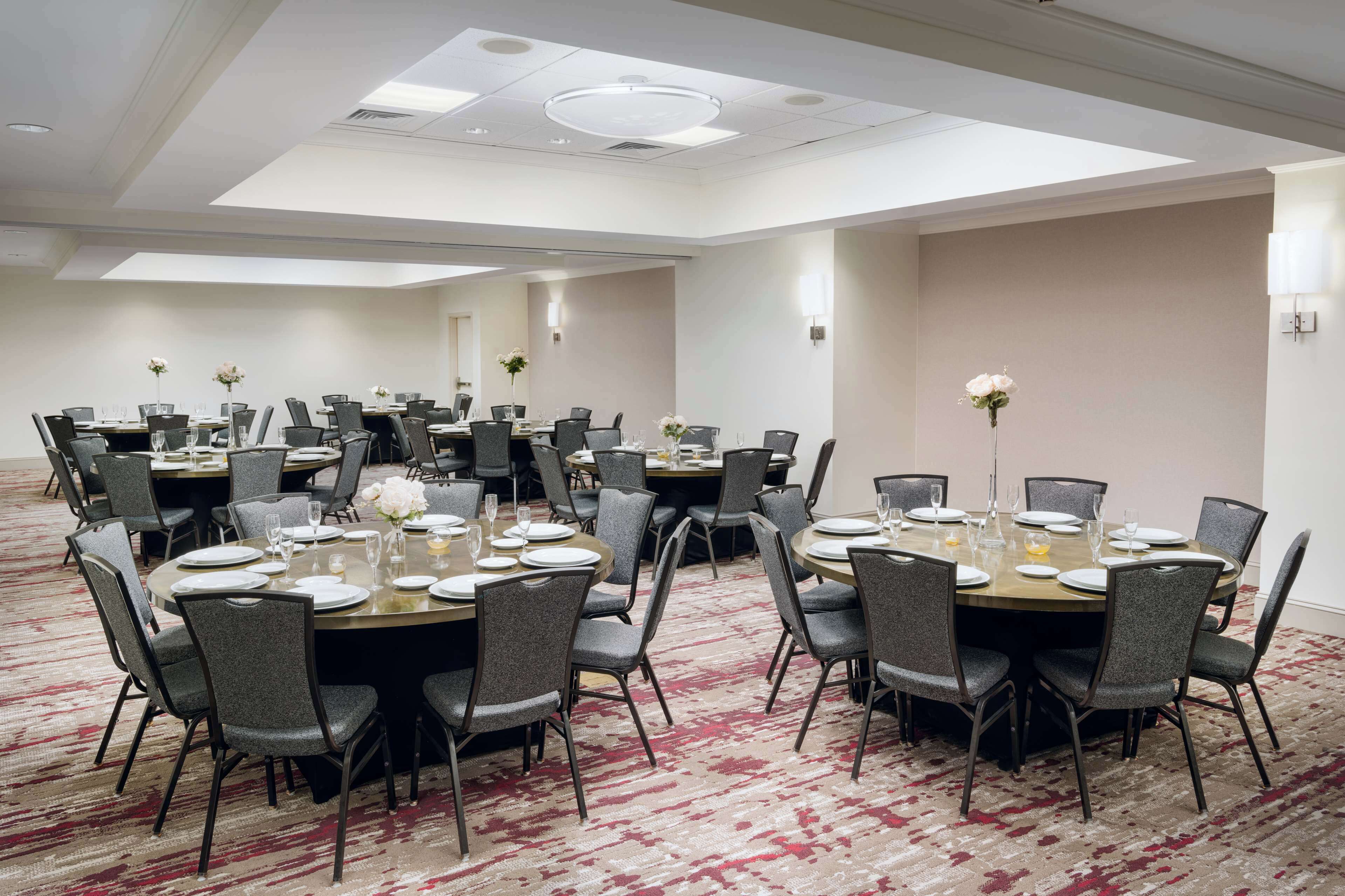 A conference room with multiple round tables, each set with chairs, plates, and glasses.