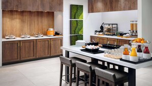 Een moderne keuken met houten kastjes, een centraal eiland met barstoelen en een ontbijtbalk met diverse etenswaren en drankjes.