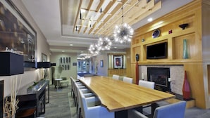 A spacious dining area with a long wooden table, white chairs, and a fireplace. - Hilton Garden Inn Toledo Perrysburg (Perrysburg)