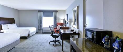 A hotel room with two beds, a desk with a computer, a chair, a microwave, and a water dispenser.