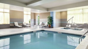 A swimming pool with lounge chairs and a sunbed, surrounded by large windows and a potted plant. - Hilton Garden Inn Toledo Perrysburg (Perrysburg)