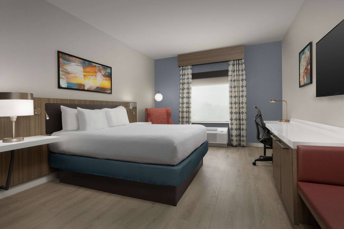 A modern hotel room with a large bed, a desk, a chair, and a TV.
