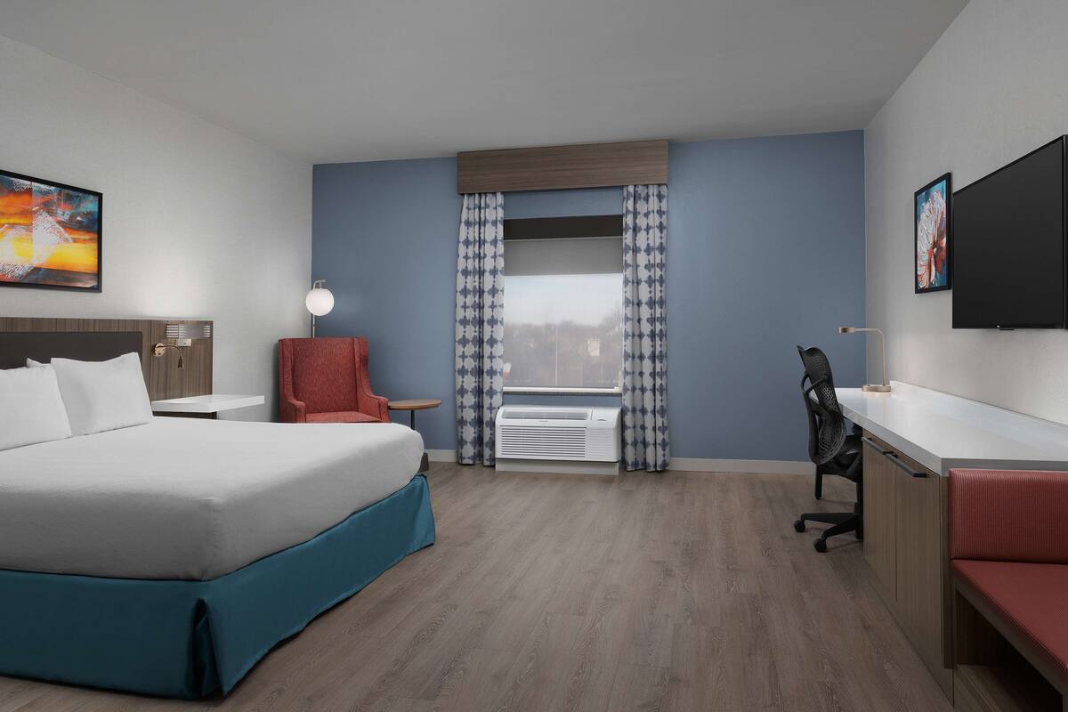 A hotel room with a bed, desk, chair, and a large window with curtains.