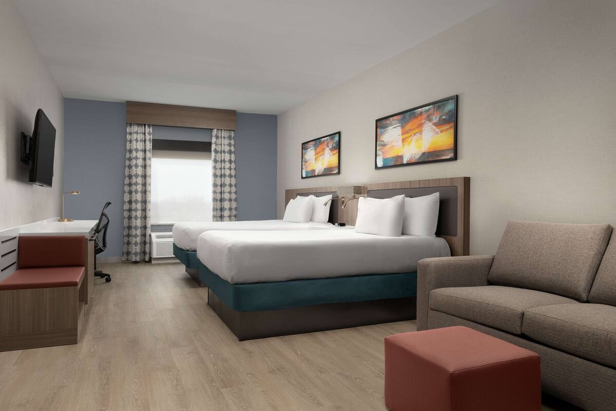 A modern hotel room with a bed, a desk, a sofa, and a TV.
