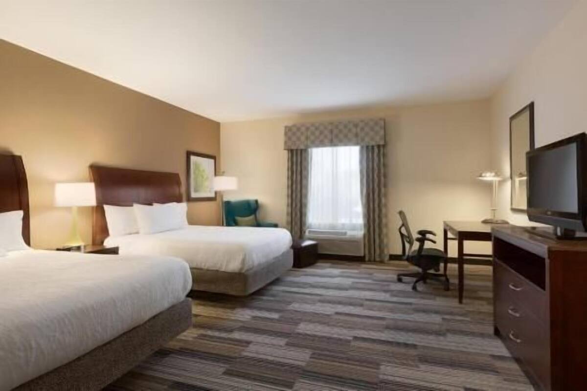 A hotel room with two beds, a desk, a chair, a television, and a window with curtains.