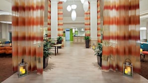 A hotel lobby with a central reception desk, potted plants, and a chandelier. - Hilton Garden Inn Casper (Casper)