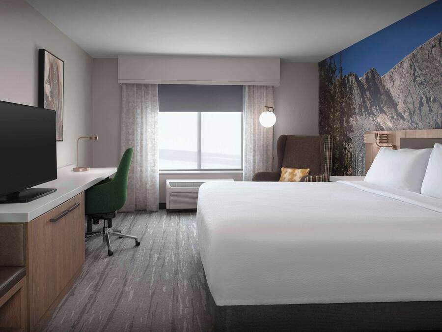 A hotel room with a bed, desk, chair, TV, and a large window with curtains.